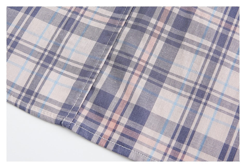 Close-up of stitching along the hem of a beige, navy, gray, and pale blue plaid garment.