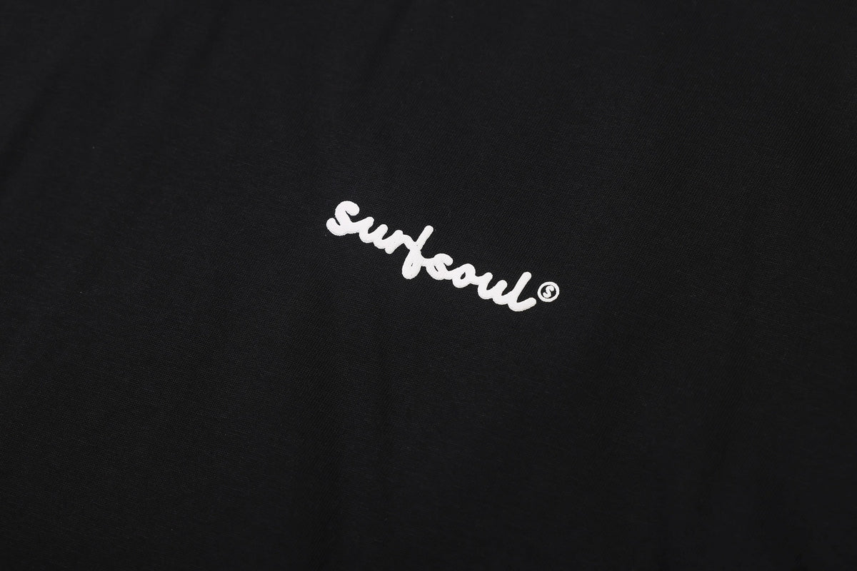 Close-up of a small white cursive “Surf soul” print on black T-shirt fabric.
