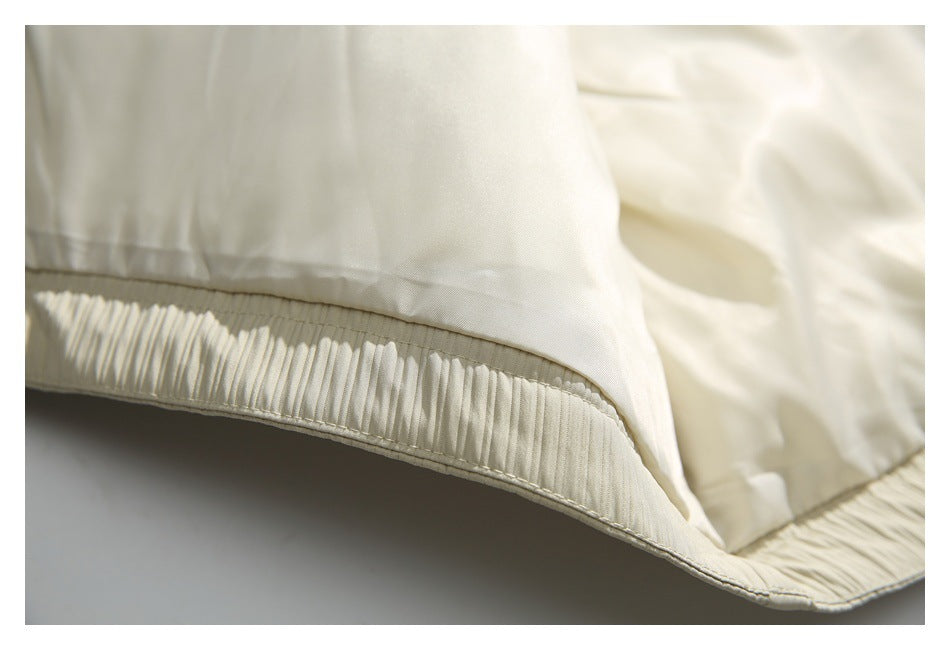 Close-up of smooth ivory lining above a finely gathered, pleated garment hem.