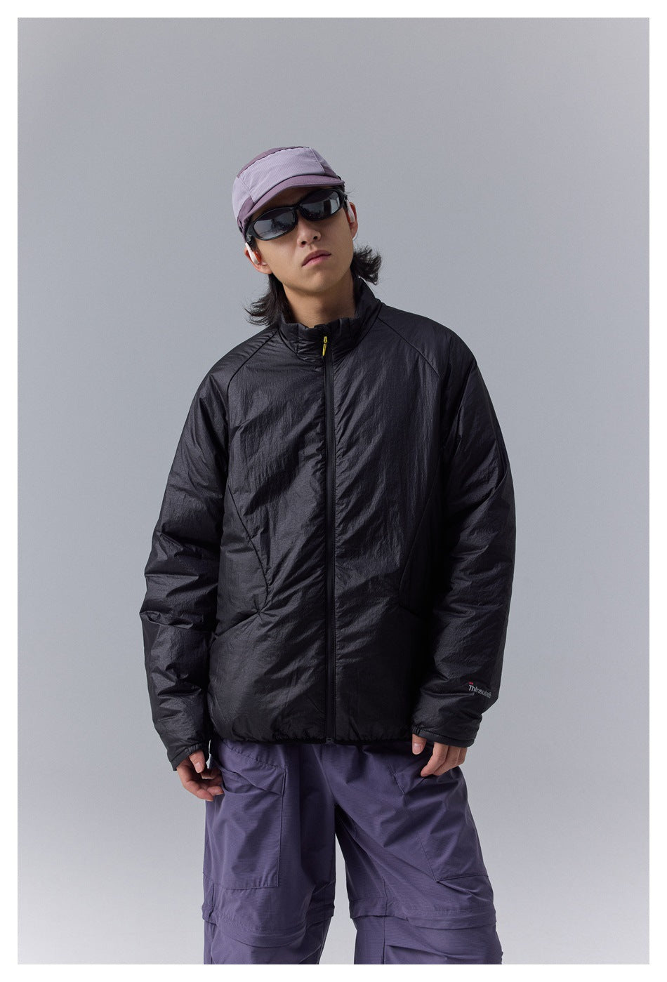 Closer front view of a model wearing a black high-collar zip jacket with purple cargo pants.
