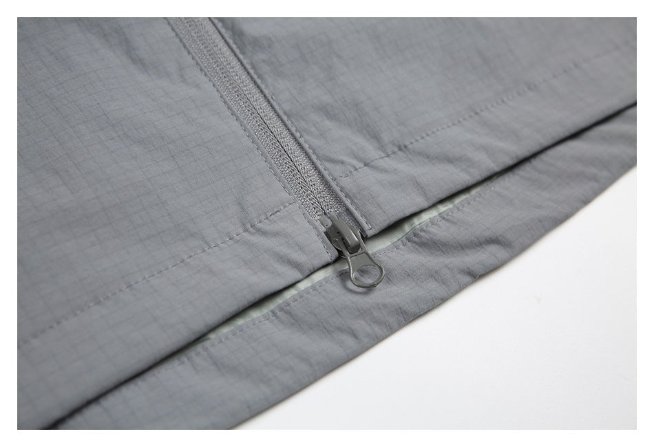 Close-up of the gray jacket's front zipper slider and stitched hem, with a narrow pale sage layer beneath.