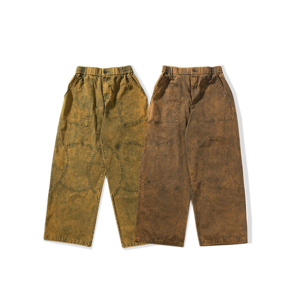 Two pairs of wide-leg trousers shown from the front in mottled olive ochre and brown, with large curved leg panels.