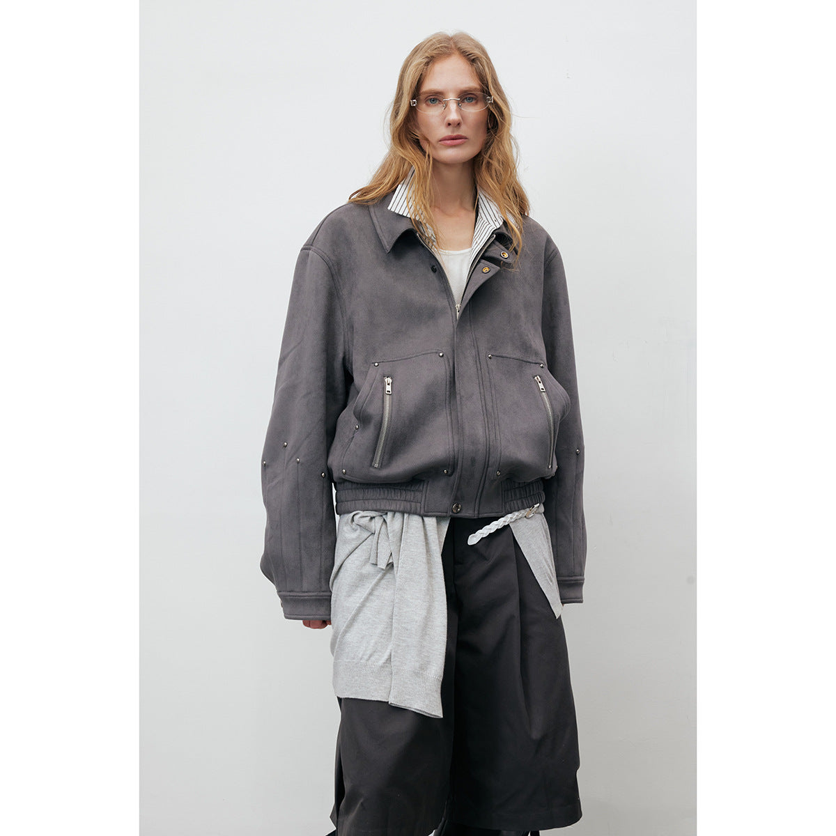 Front view of a model in a charcoal gray jacket with zip pockets, metal studs, and a gathered hem.