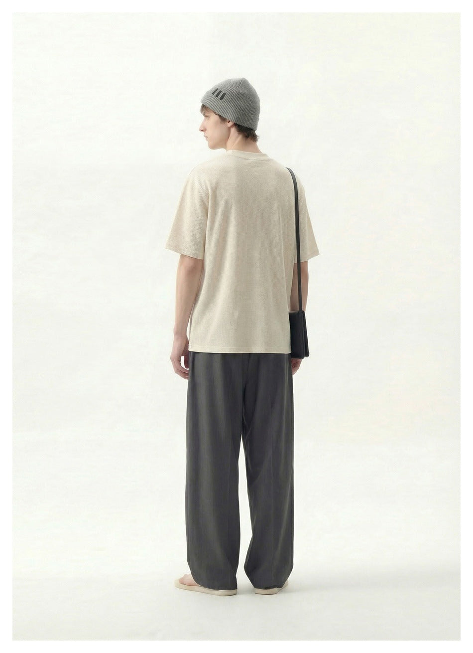 Rear view of a model wearing a cream T-shirt, gray beanie and charcoal wide-leg trousers.