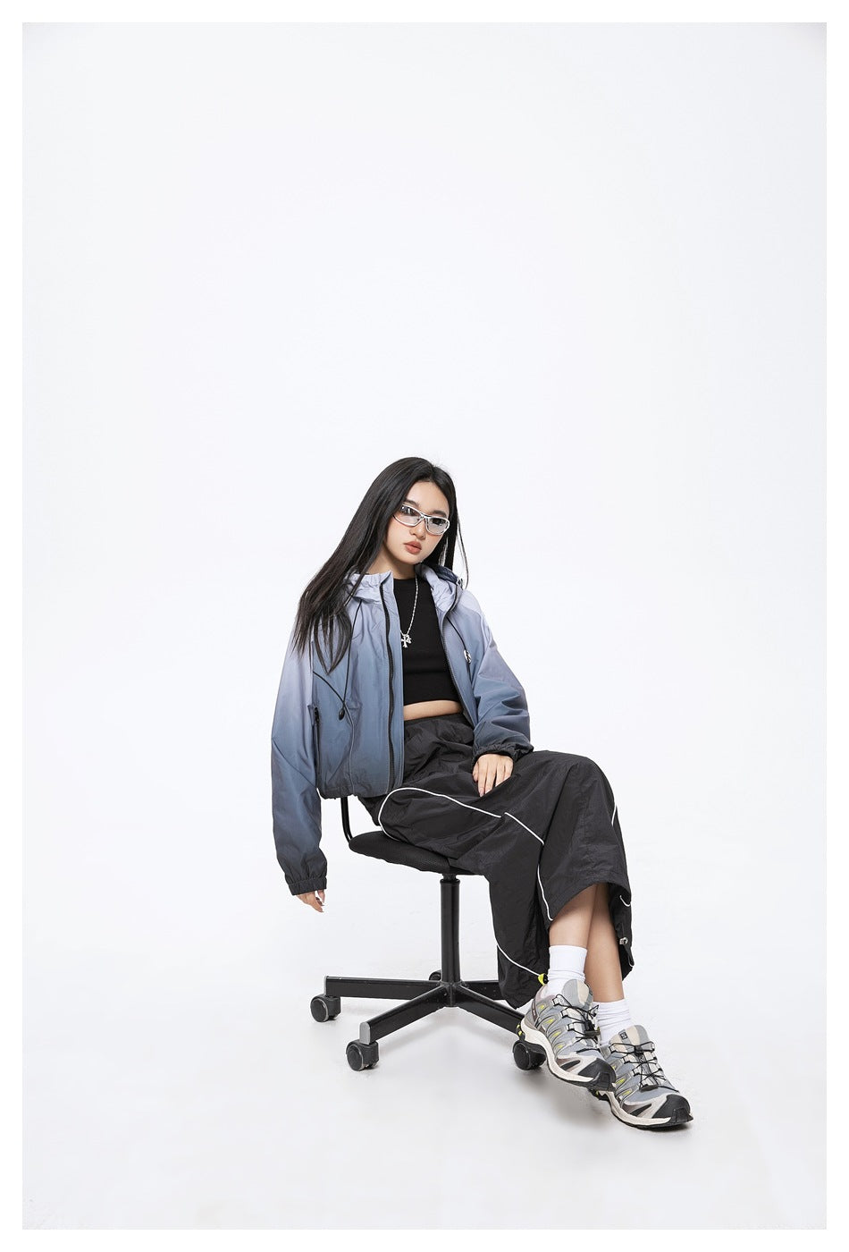Model seated in a blue-gray gradient hooded jacket with a black top and pants.