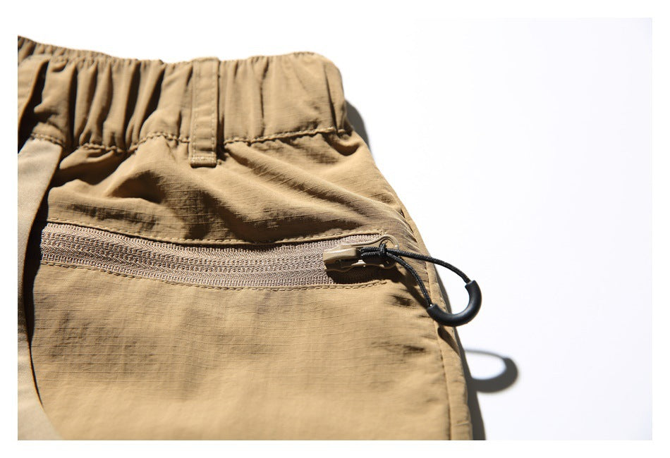 Close-up of a horizontal zipper pocket and cord loop pull on tan utility shorts.