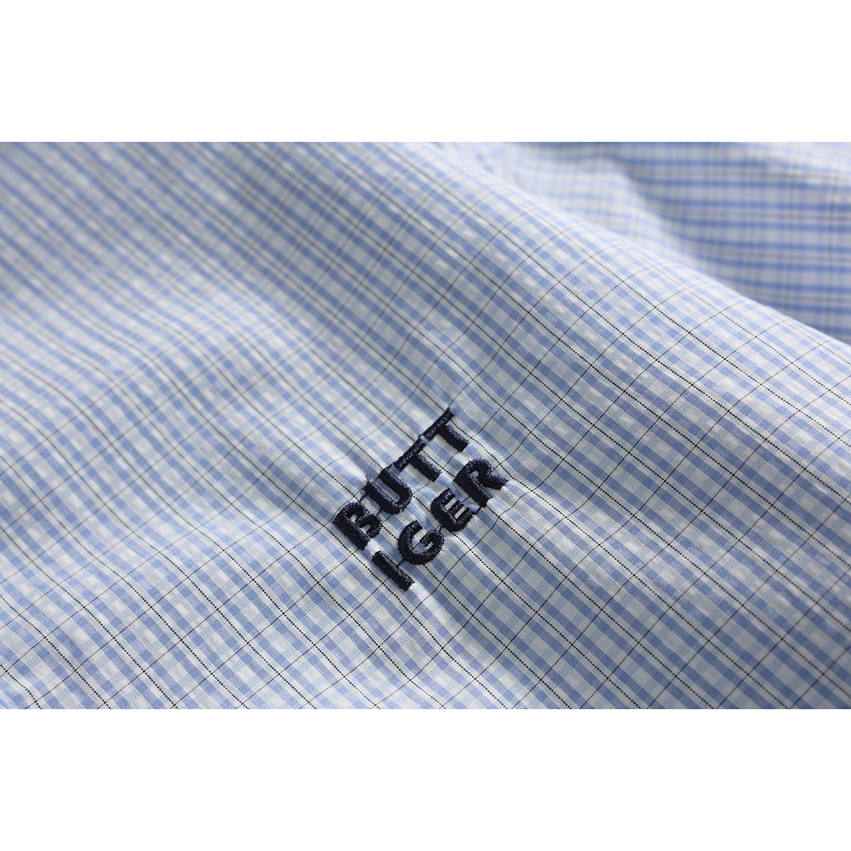 Close-up of dark embroidered lettering on the blue-and-white checked shirt fabric.