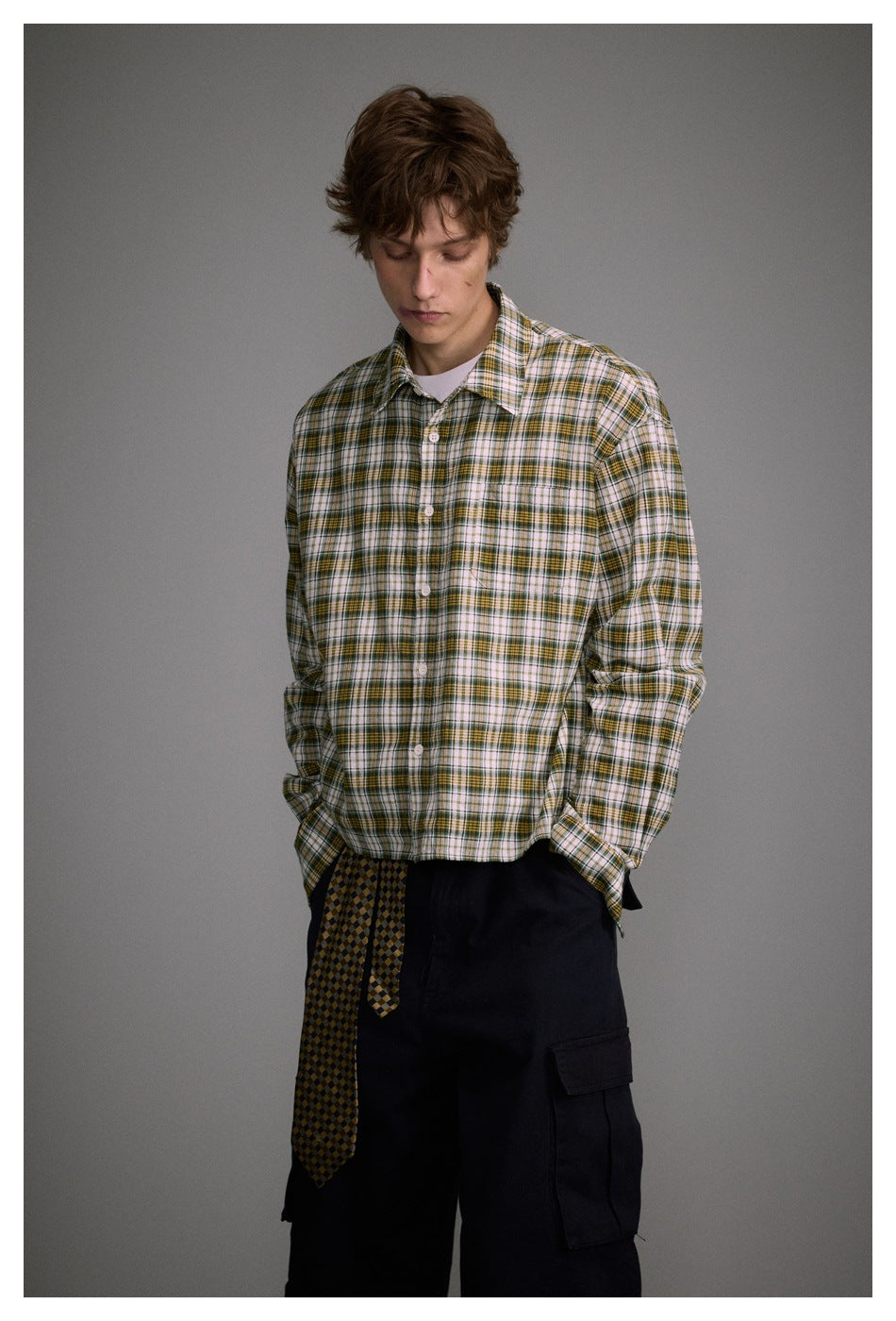 Model wearing a white, green, and mustard plaid button-up shirt with dark cargo pants.