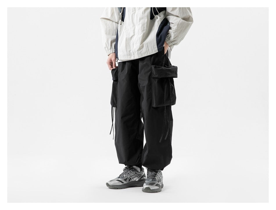 Person wearing black cargo pants with large flap pockets and strap details, with a light jacket and gray sneakers