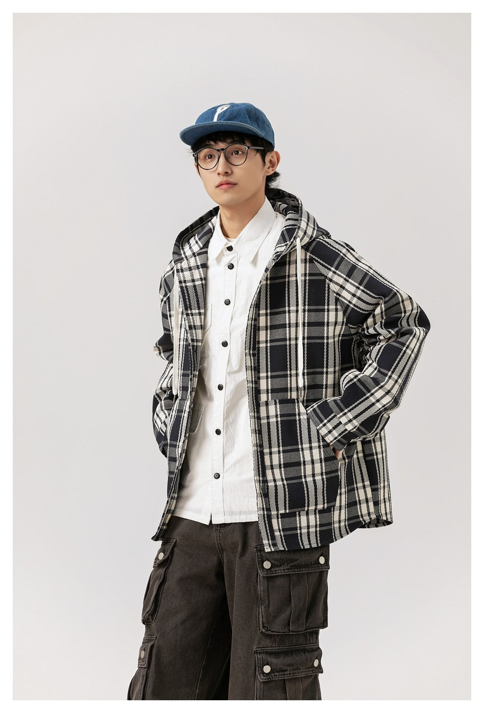 Model posing in an open black-and-white plaid hooded jacket over a white shirt and dark cargo pants.