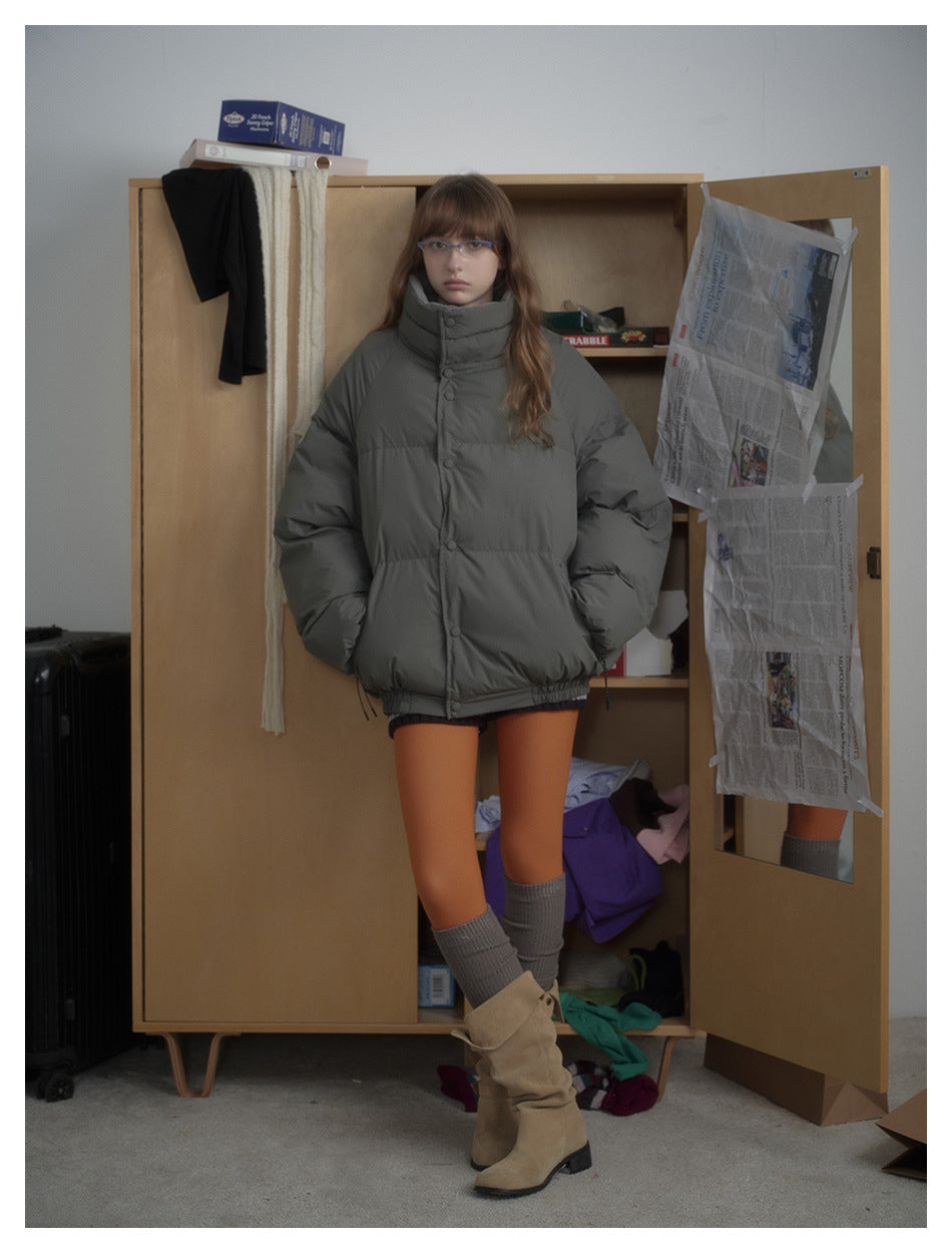 Front view of a model wearing a charcoal-gray puffer jacket with a tall padded collar and snap front.