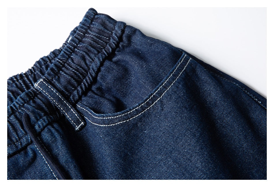Close-up of dark indigo denim shorts showing the elastic waistband, belt loop, and curved front pocket.
