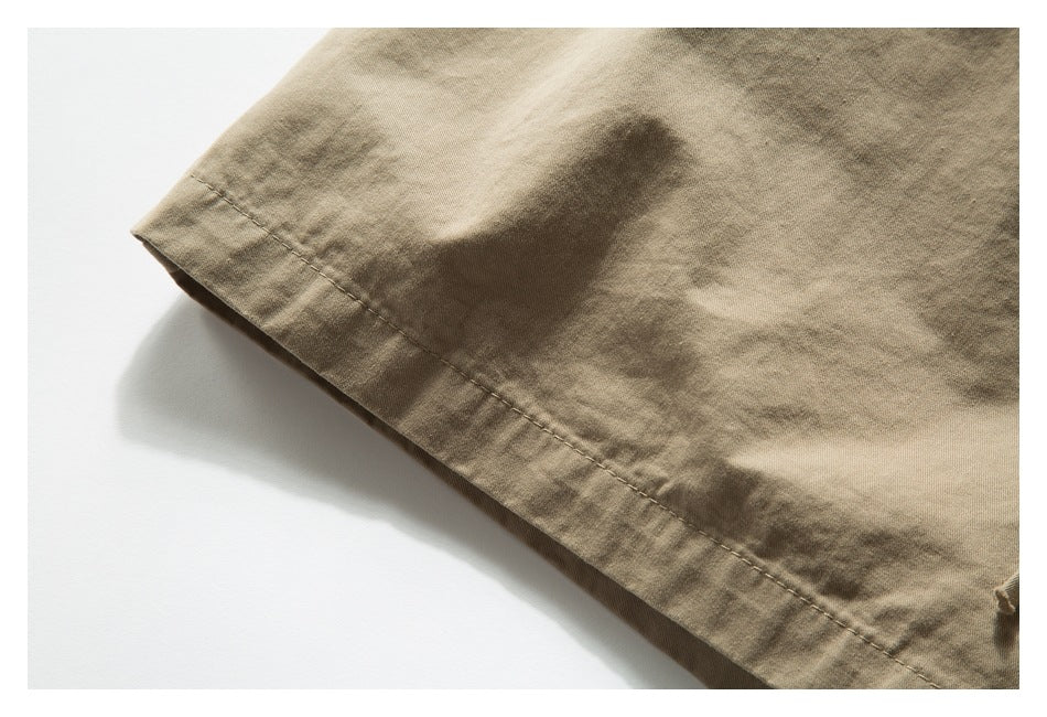 Close-up of the stitched hem on beige shorts against a white background.