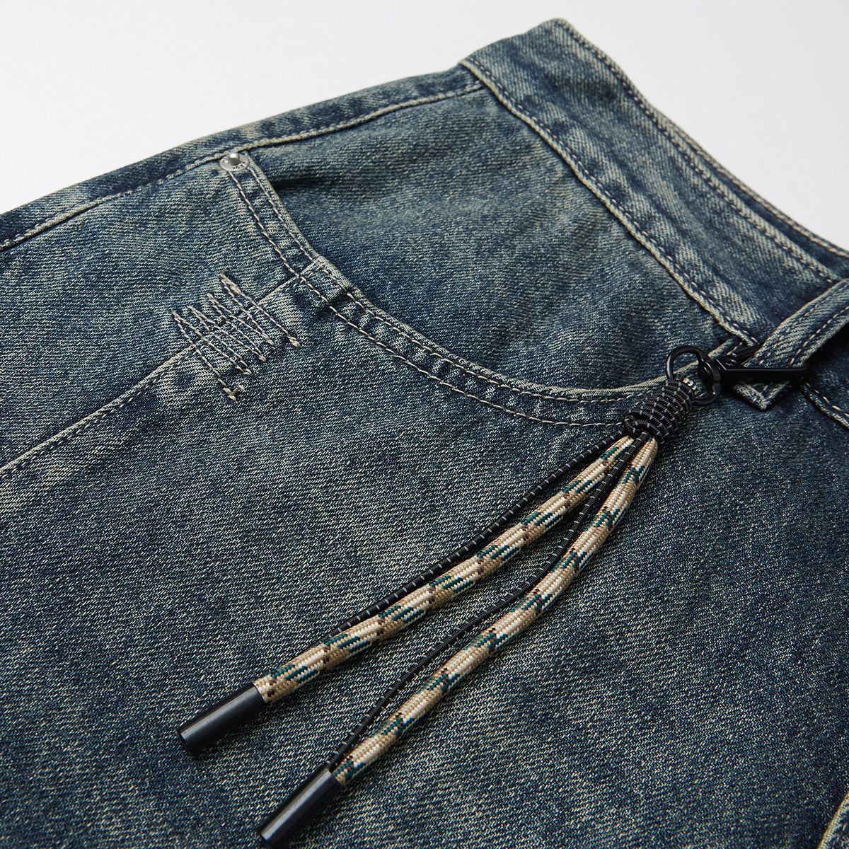 Close-up of dark washed jeans showing the waistband, coin pocket stitching and patterned drawstrings.