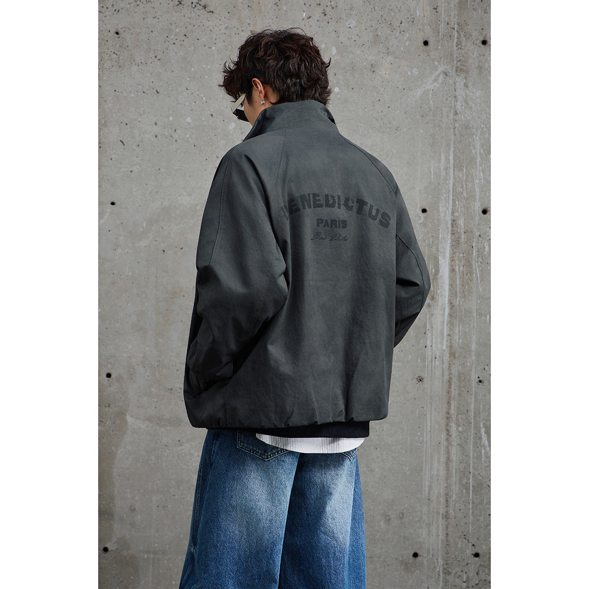 Rear view of a person wearing a charcoal jacket with dark lettering across the back.