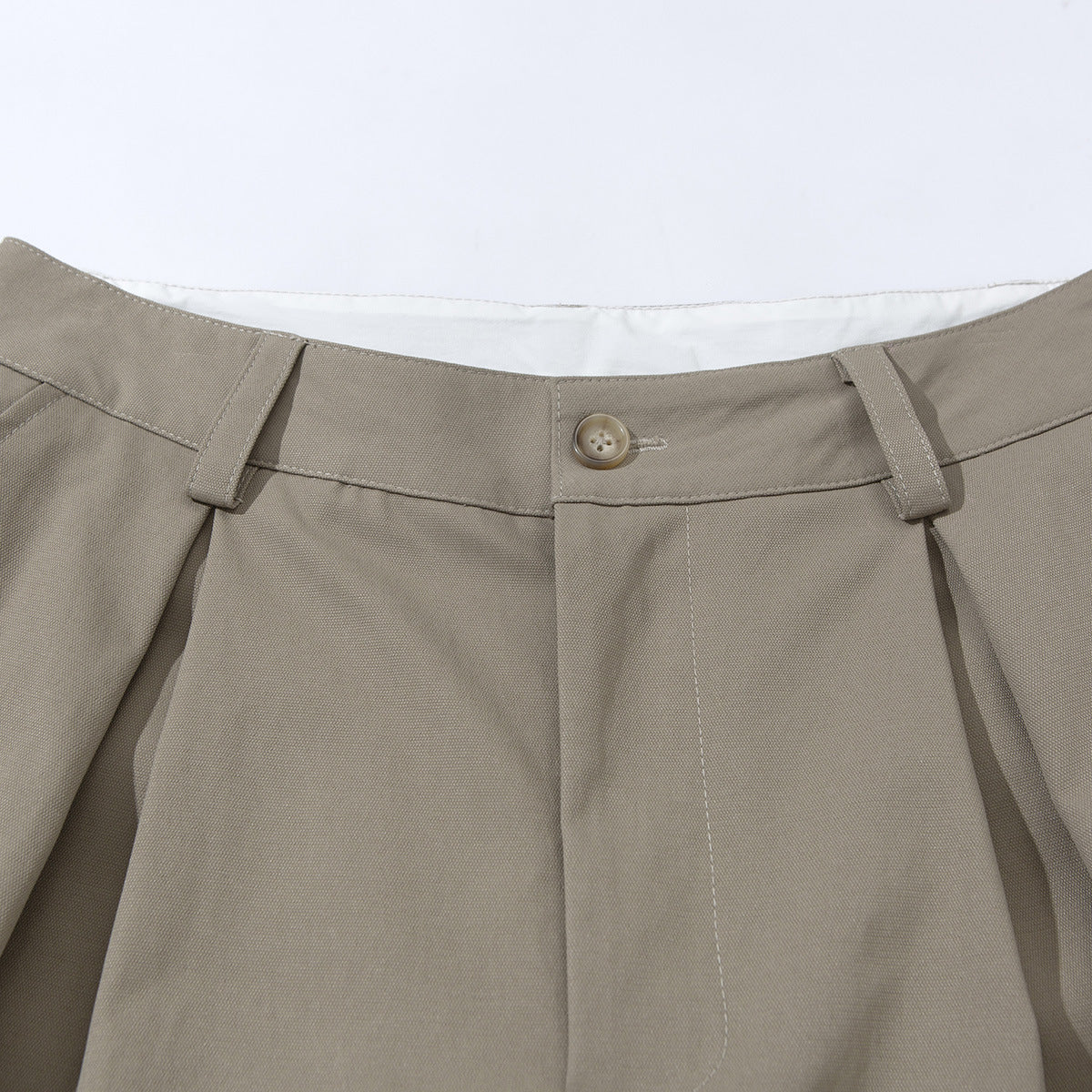 Close-up of taupe tailored shorts showing the waistband, button, belt loops, and front pleats.