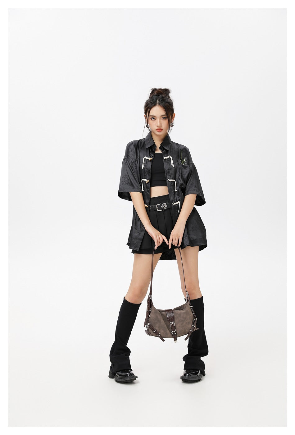 Model wearing the black short-sleeve rope-closure shirt open over a black crop top, pleated skirt and leg warmers