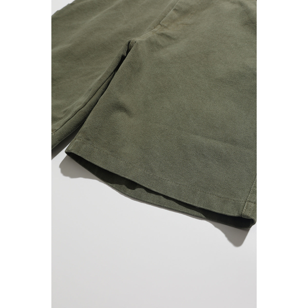 Close-up of the olive shorts' leg and stitched hem.
