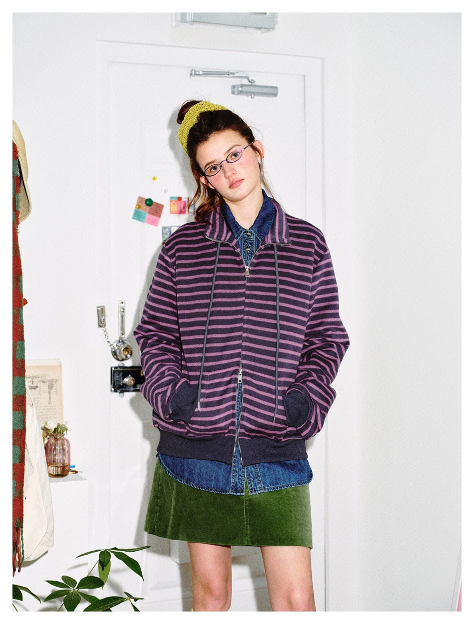 Model wearing the purple striped zip jacket over a denim shirt with a green corduroy skirt, hands in pockets