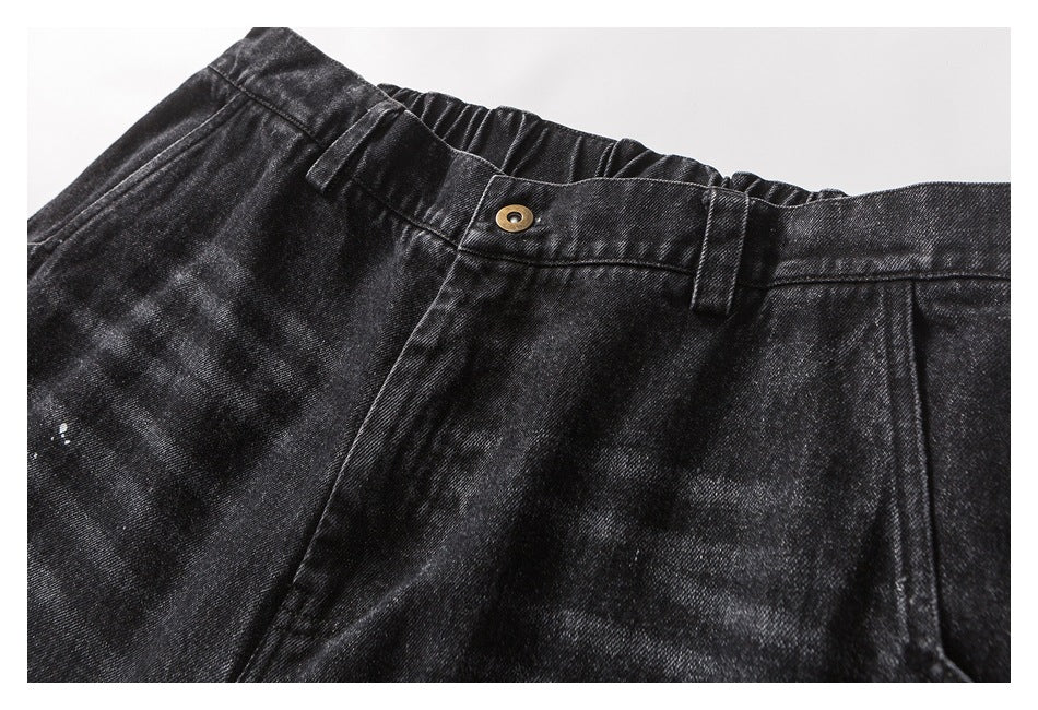 Close-up of the front waistband and button on black washed trousers with subtle white paint marks.