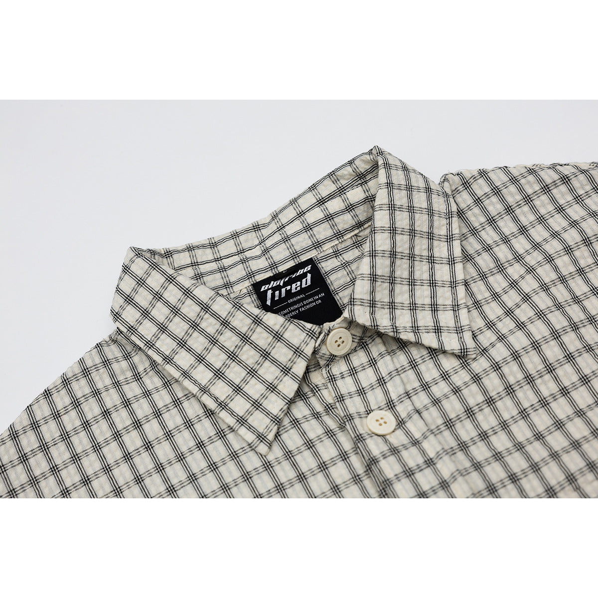 Close-up of a cream short-sleeve shirt with a black windowpane check, pointed collar, and light buttons.