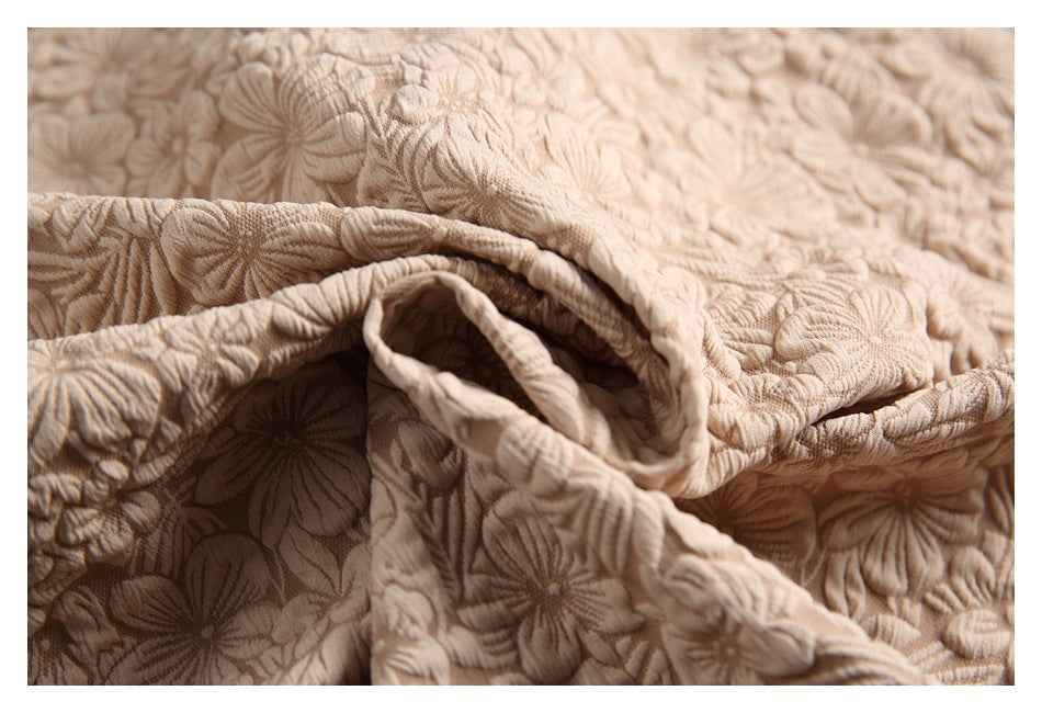 Close-up of beige fabric with a raised floral pattern and folded, stitched edge.