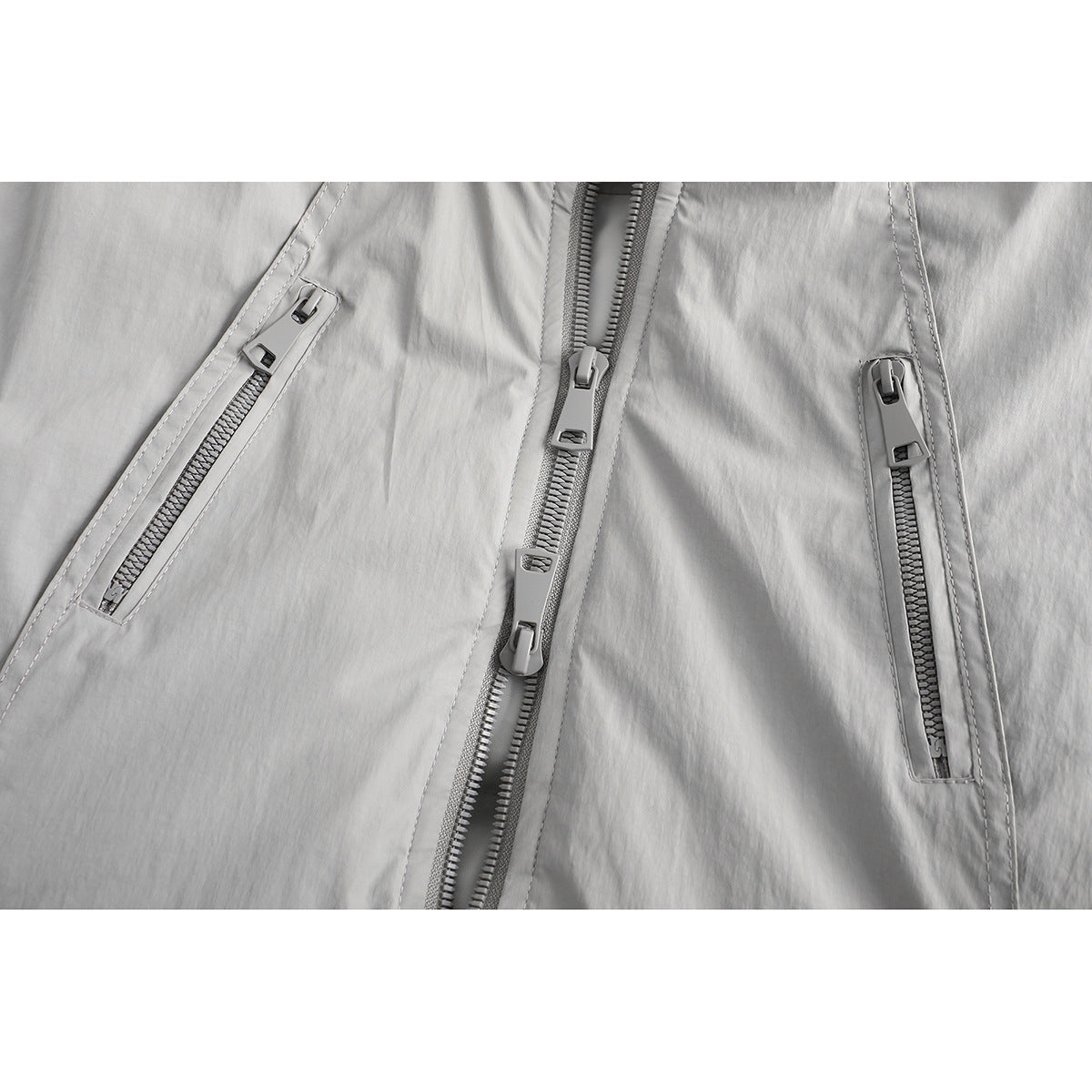 Close-up of a light gray jacket front with a central zipper and two angled zip pockets.