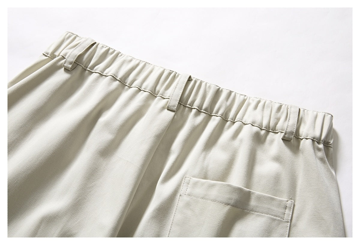 Close-up of cream trousers with an elastic waistband, belt loops, and a rear patch pocket.
