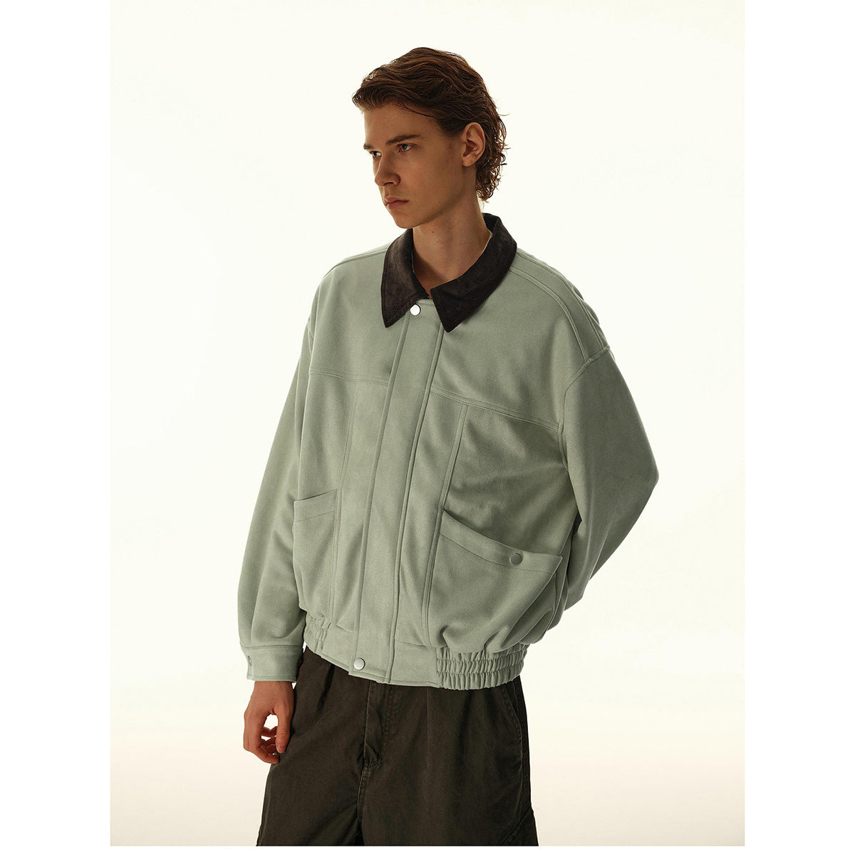 Man wearing a sage green jacket with a dark collar, front pockets, and an elasticated hem.