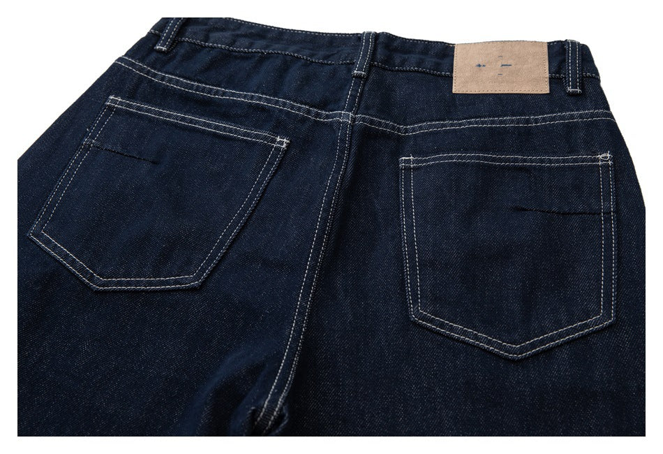 Rear view of dark indigo jeans showing two stitched back pockets and a tan waistband patch.