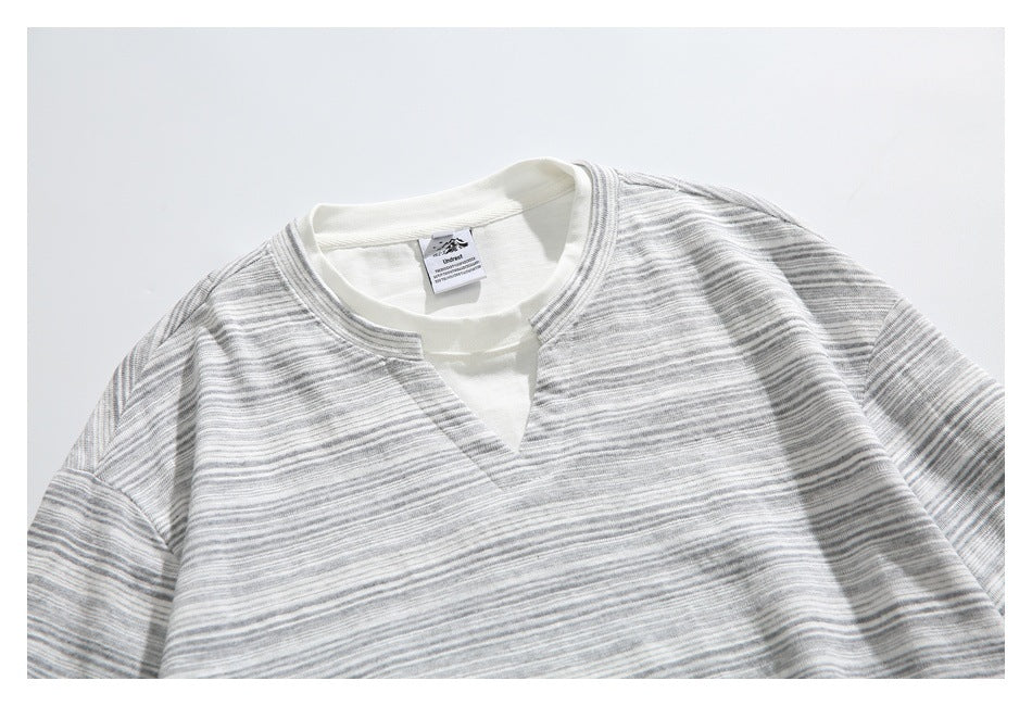 Close view of a gray-and-white striped long-sleeve top with a cream crew neckline and small V-shaped front opening.