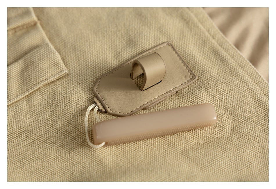 Tan plastic toggle and stitched leather-like tab on beige woven fabric.