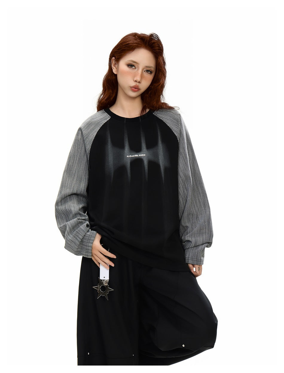 Model wearing an oversized black top with gray pinstriped raglan sleeves and small white chest lettering, paired with wide