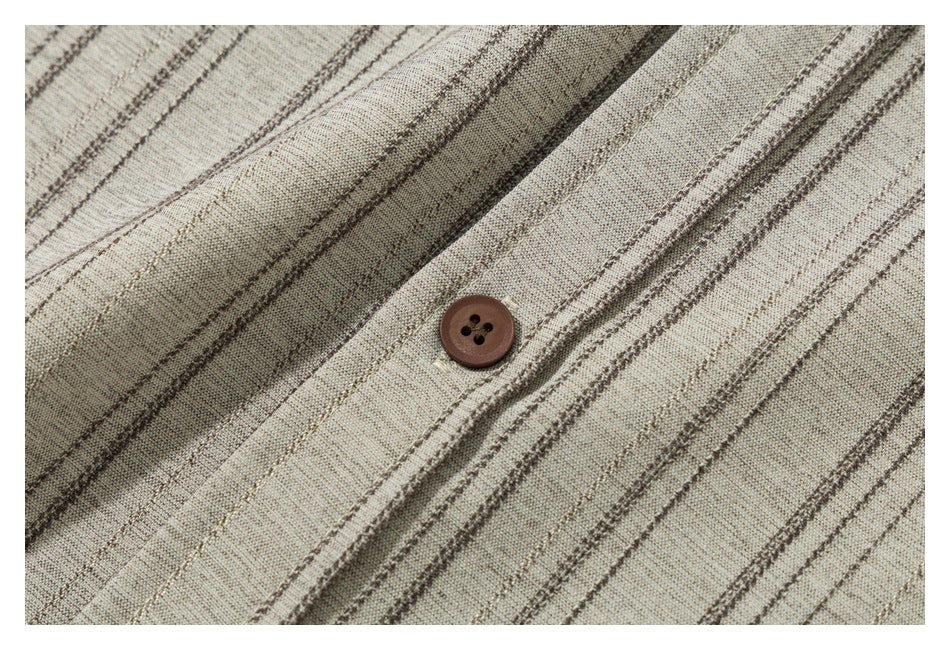Close-up of a brown four-hole button on the placket of a beige shirt with thin dark stripes.