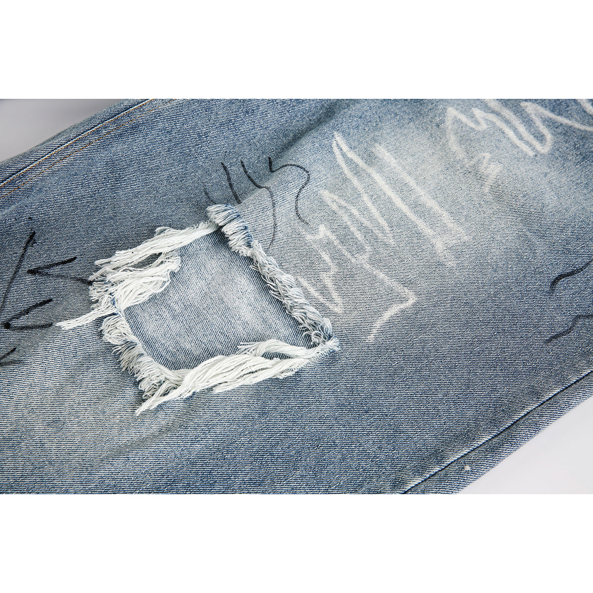 Close-up of a frayed rectangular hole and decorative markings on faded blue denim shorts.