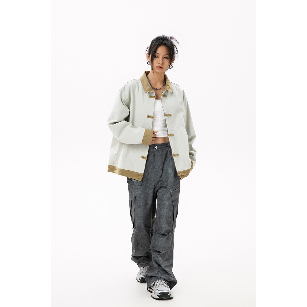 Model wearing an oversized pale gray jacket with tan trim and toggle closures, paired with dark wide-leg cargo pants.