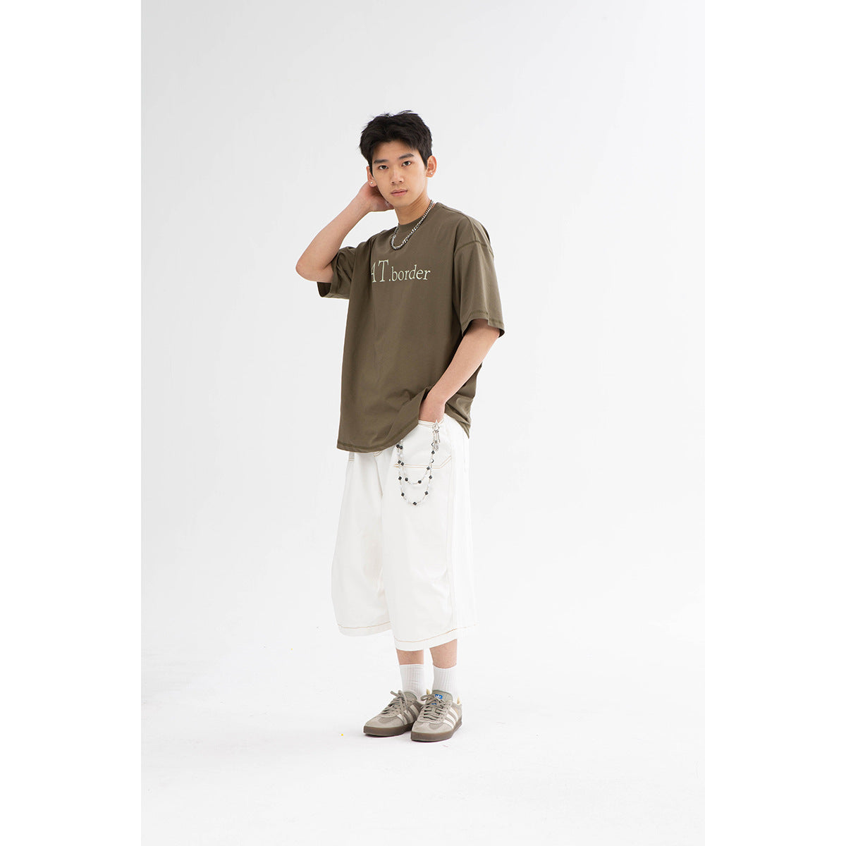 Model wearing an oversized olive-brown T-shirt with pale lettering and white knee-length shorts.