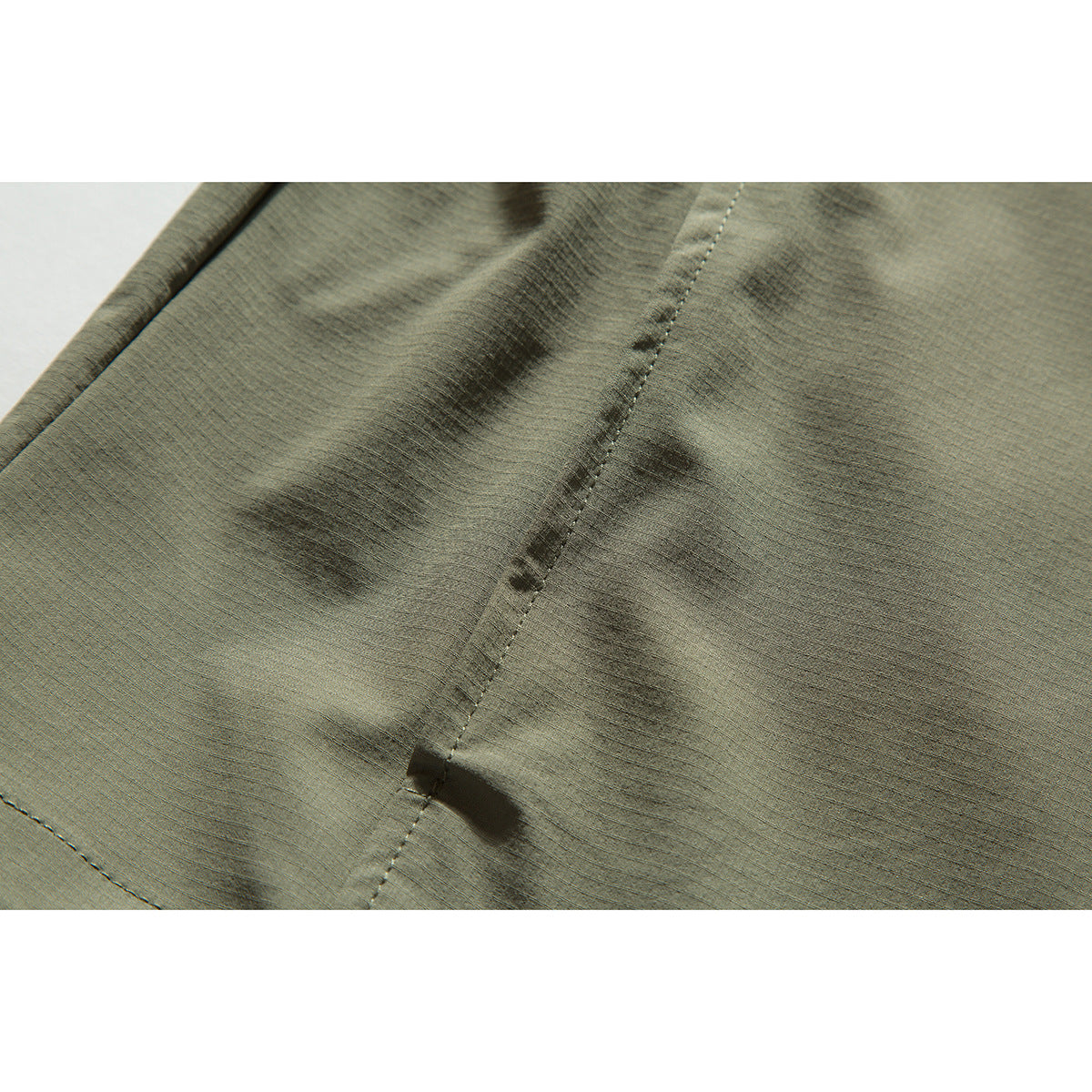 Close-up of olive-gray jacket fabric, a stitched seam, and a small black tab.