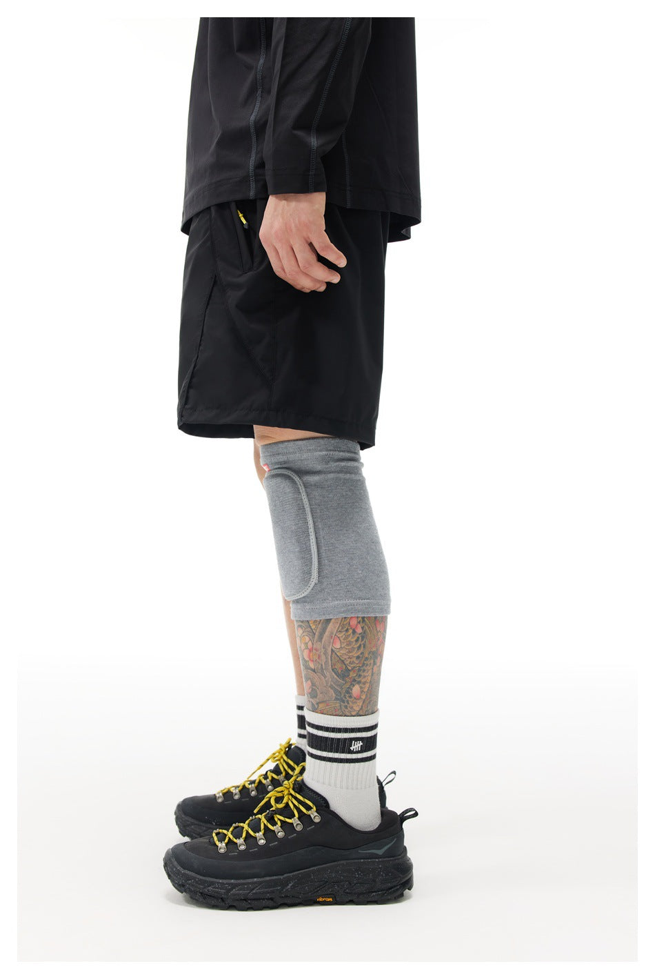 Side view of a person wearing black shorts with a black long-sleeve top, gray knee sleeve and black hiking shoes