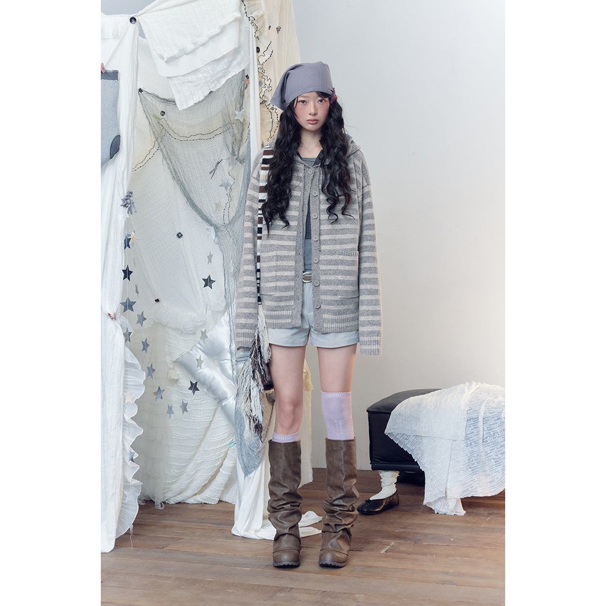 Full-length model wearing a gray striped hooded cardigan over a striped top with pale shorts and brown boots.