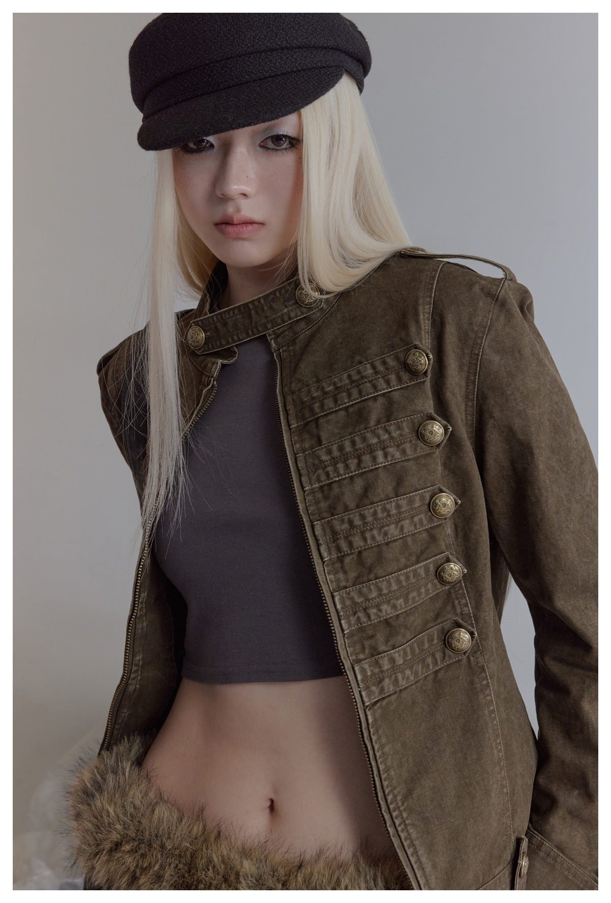 Close-up of an olive-brown jacket on a model, showing its stand collar, decorative brass buttons, and front zipper.