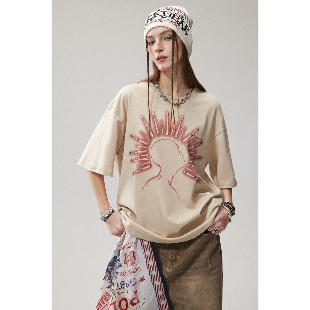 Model wearing an oversized beige T-shirt with a pink radiating silhouette graphic and metallic studs.