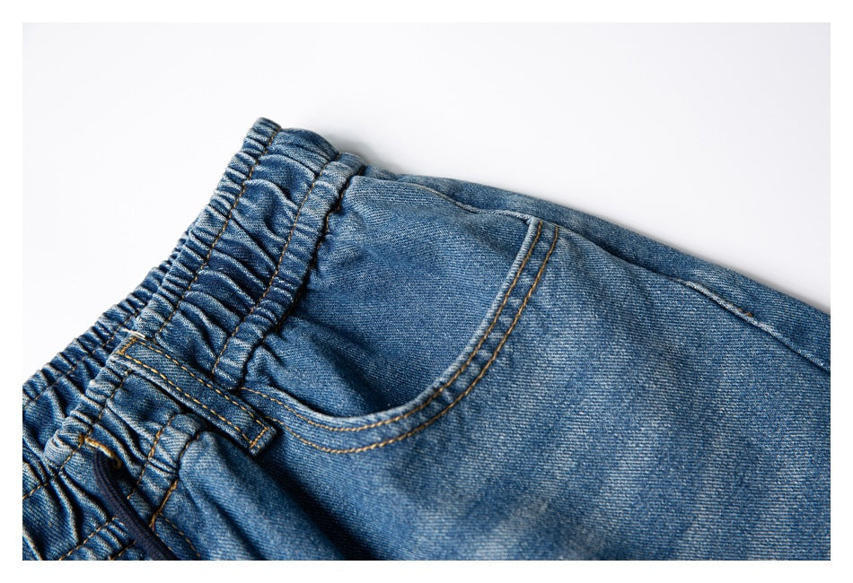 Close-up of blue denim pants showing the elastic waistband and a curved front pocket.
