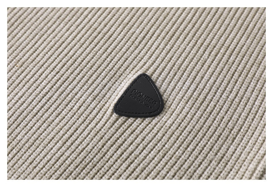 Close-up of a black triangular branded patch sewn onto cream ribbed knit fabric.