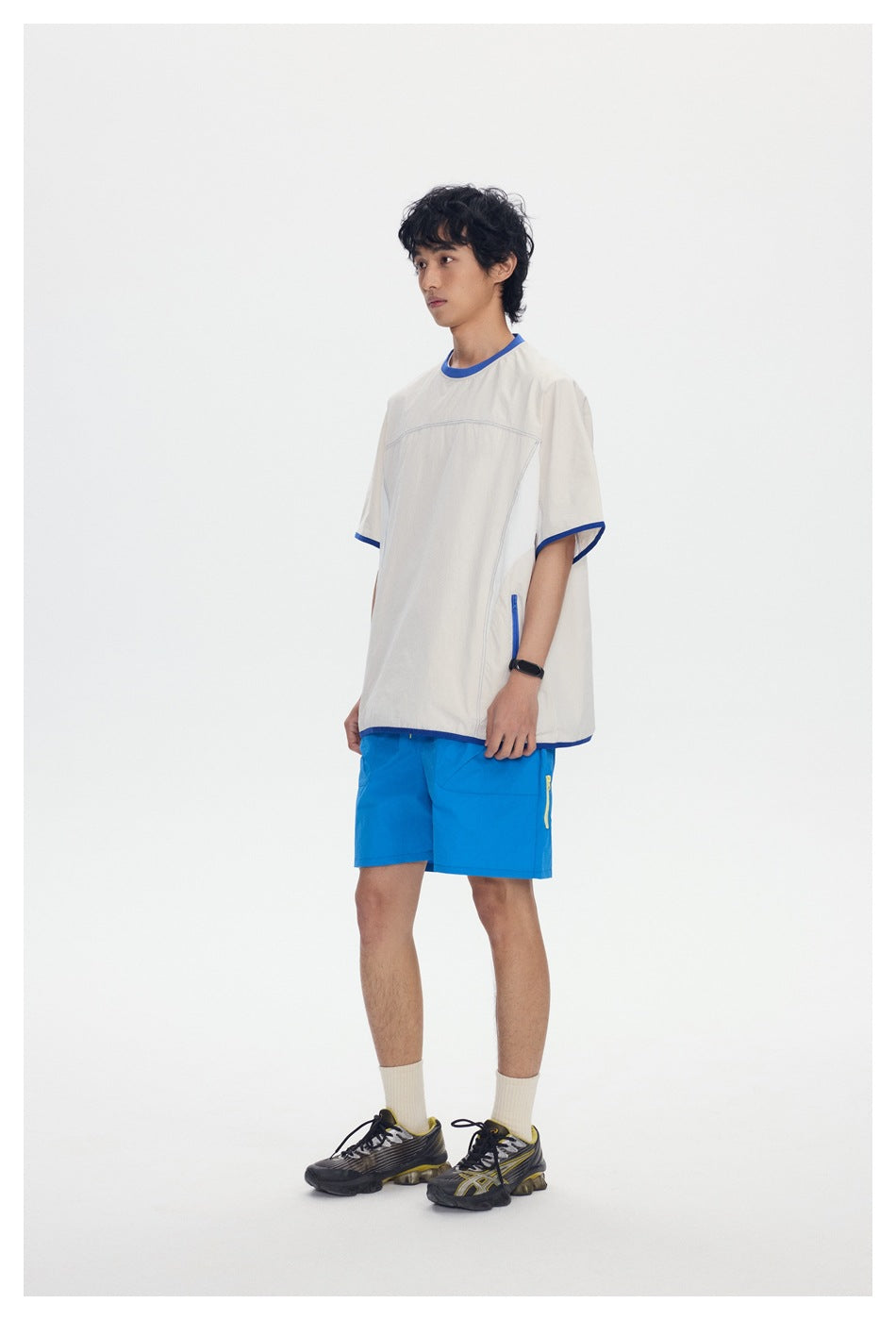 Model wearing a white short-sleeve top with blue trim and blue zippered side pocket, with blue shorts, side view
