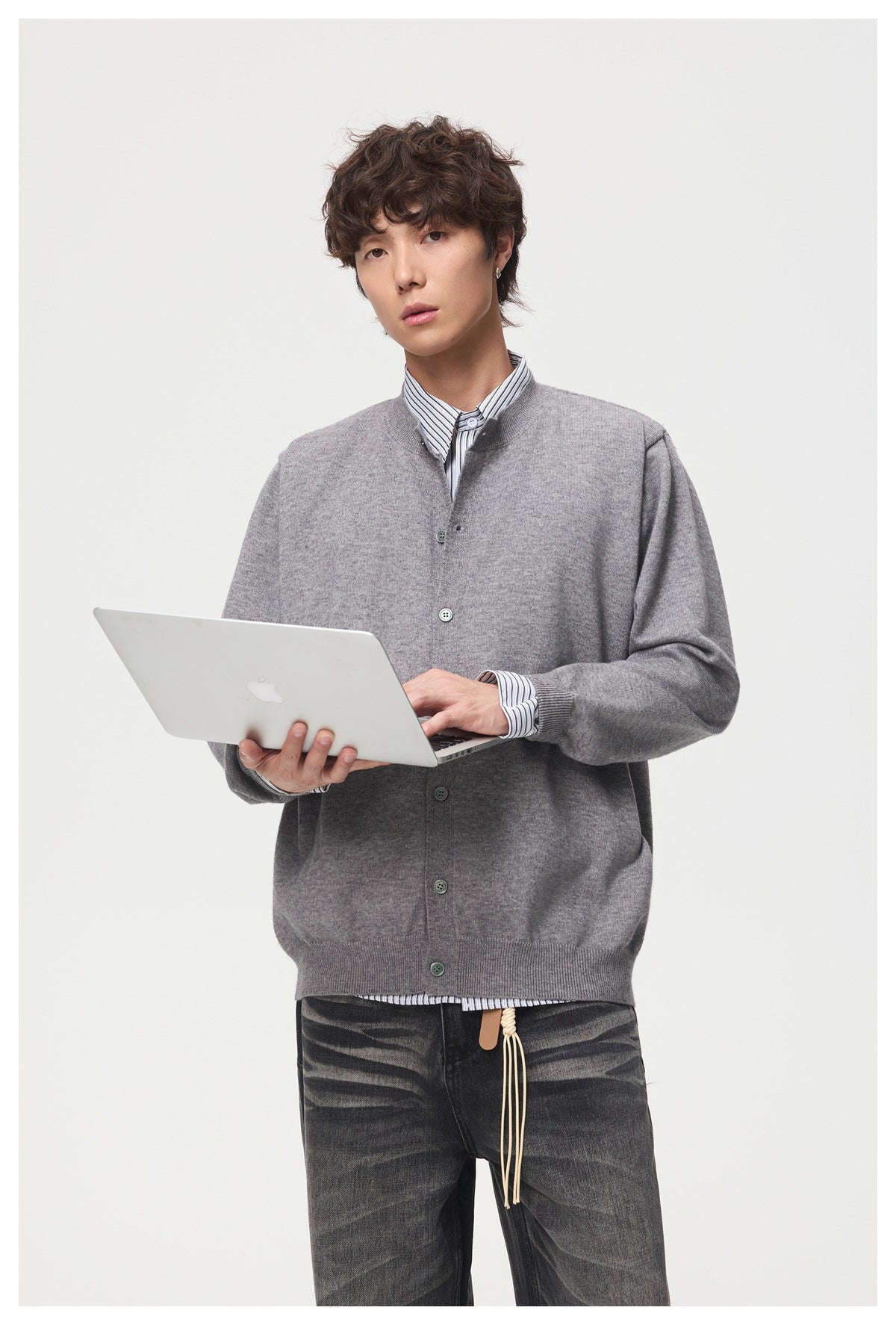Model wearing a gray button-front cardigan over a striped shirt, holding a laptop.