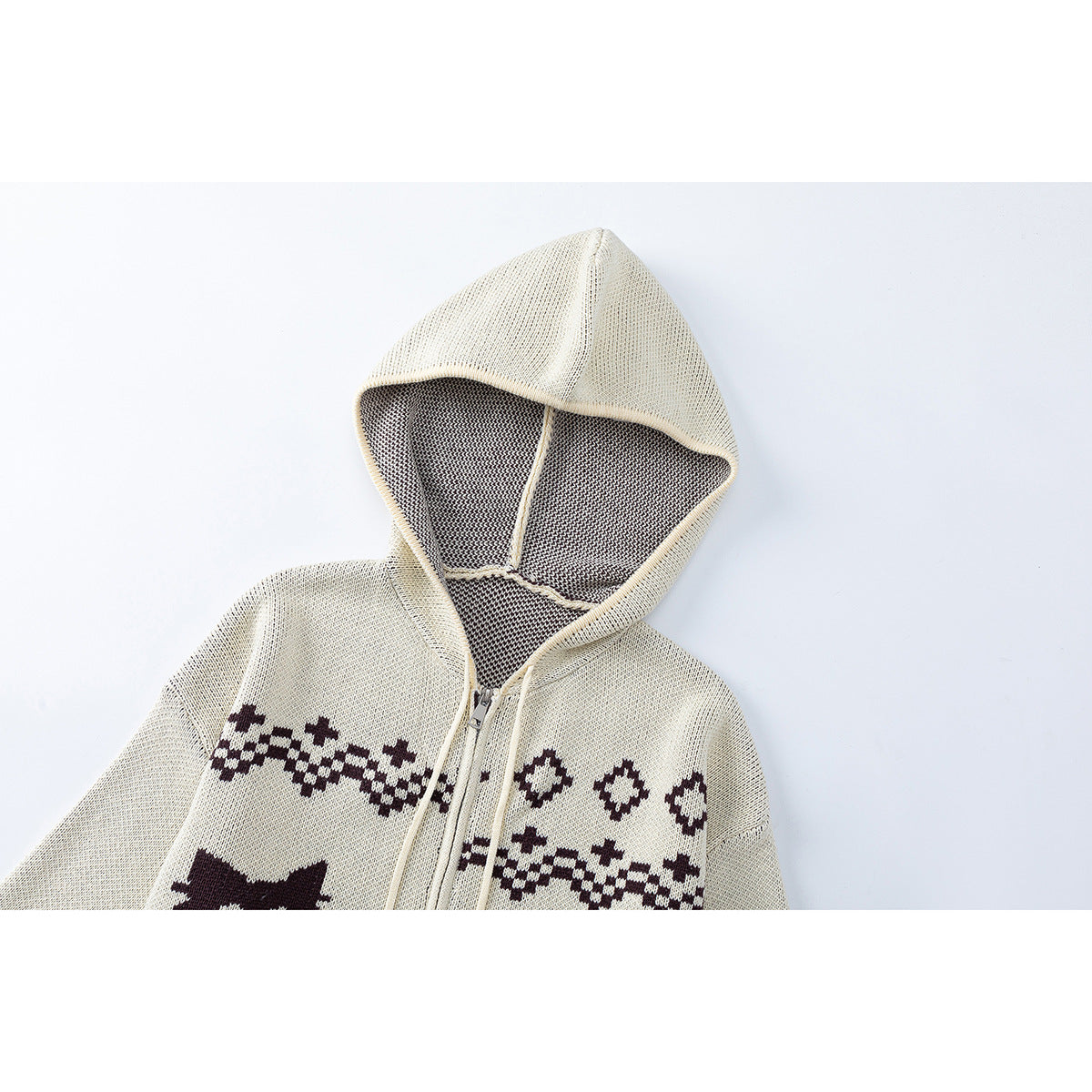 Close-up of an ivory knit zip hoodie showing its lined hood, zipper, and dark geometric chest pattern.
