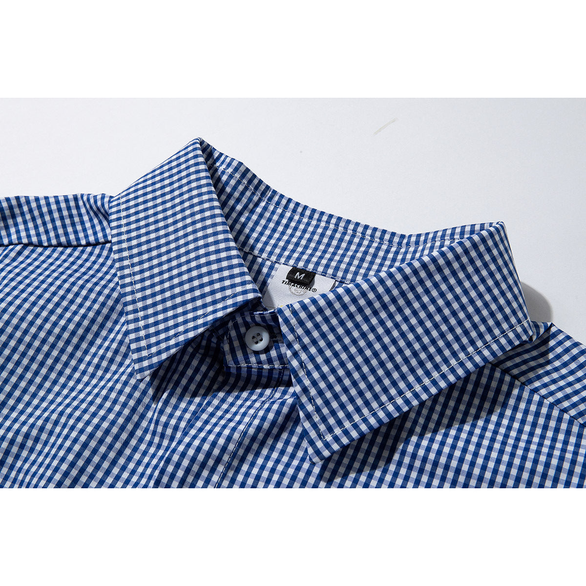 Close-up of a blue-and-white gingham shirt collar, top button, and sewn-in neck label.
