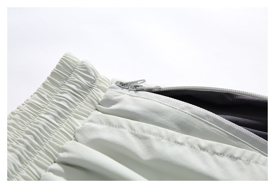 Close-up of light-colored shorts showing a zipper opening, zipper pulls and dark inner lining.
