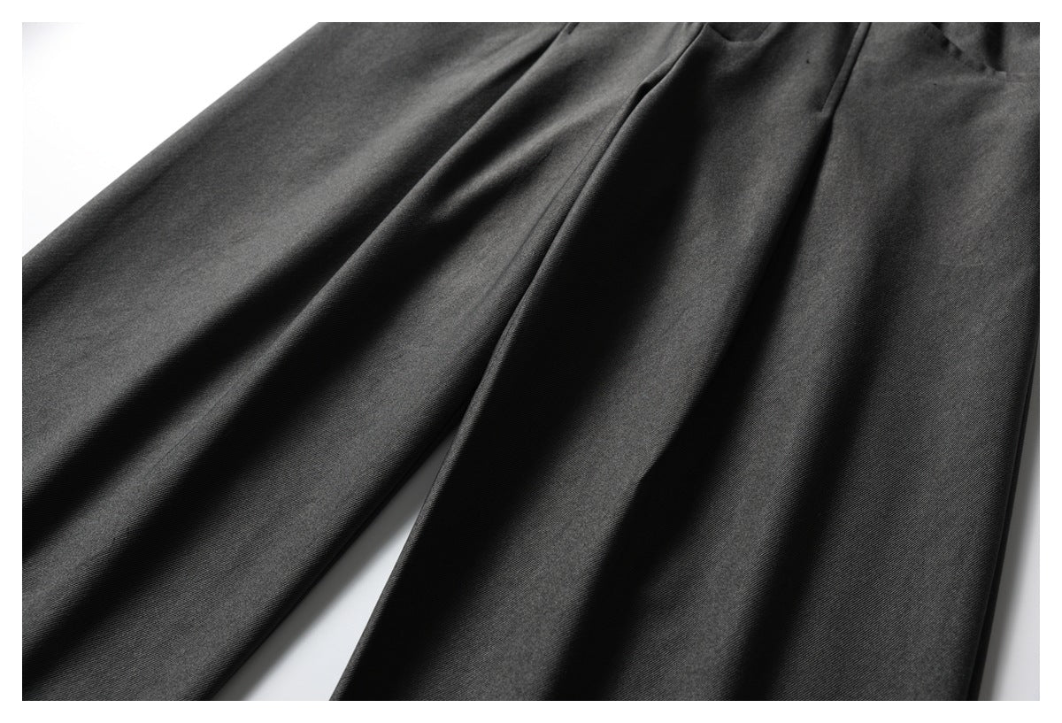 Close-up of the wide legs and front pleats of dark charcoal trousers.
